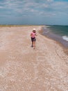 Happy child in a straw hat running jumping having fun on empty autumn sea beach. Blond girl walking on white sand