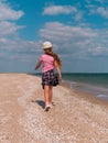 Happy child in a straw hat running jumping having fun on empty autumn sea beach. Blond girl walking on white sand