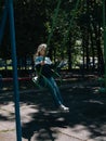 Happy child on a swing in sping park. Cute little girl with long hair swinging on a playground alone in tree shadow Royalty Free Stock Photo