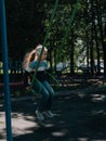 Happy child on a swing in sping park. Cute little girl with long hair swinging on a playground alone in tree shadow Royalty Free Stock Photo