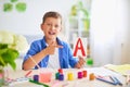 Happy child at the table with school supplies smiles funny and learns the alphabet in a playful way.positive student in a bright
