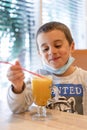 Happy child wearing a mask in a cafe during a pandemic. A boy in a cafe drinks sea buckthorn tea in a cafe during a pandemic