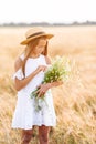 Happy child in wheat field. Beautiful girl in white dress in a straw hat with ripe wheat in hands
