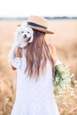 Happy child in wheat field. Beautiful girl in white dress in a straw hat with ripe wheat in hands