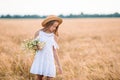 Happy child in wheat field. Beautiful girl in white dress in a straw hat with ripe wheat in hands