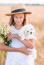 Happy child in wheat field. Beautiful girl in white dress in a straw hat with ripe wheat in hands