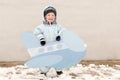 Happy child in winter fashion clothes posing with a toy airplane in the courtyard of his village house. First snow, family, tradit