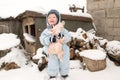 A happy child in winter fashion clothes posing with a toy pig in the courtyard of his village house. First snow, family, tradition