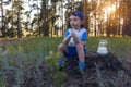 Happy childhood. Cheerful kid is drinking milk at the nature. Scenic view of the green meadow at sunset in the forest