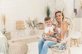 Happy childhood concept. Mother and son relationship. European beautiful blond woman sitting on boho indoor swing with Royalty Free Stock Photo