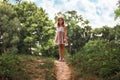 Happy childhood. Cute little schoolgirl girl in a straw hat and dress posing on a slope. Park and sky at the background Royalty Free Stock Photo