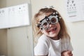 Happy childhood. Focused portrait of little girl in phoropter looking straight into the camera and smiling