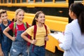 Happy children boarding school bus while black female teacher updating check list Royalty Free Stock Photo