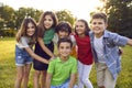 Happy children boys and girls from elementary school stand around friend on lawn summer park Royalty Free Stock Photo