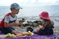 happy children brother and sister sit by the sea, have a picnic, eat fruit, pastries, drink juice and cocktail. Friends