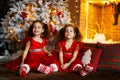 Happy children sitting on the floor near a Christmas tree and a fireplace. Smiling twin sisters in red dress hug each other Royalty Free Stock Photo