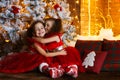 Happy children sitting on the floor near a Christmas tree and a fireplace. Smiling twin sisters in red dress hug each other Royalty Free Stock Photo