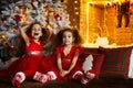 Happy children sitting on the floor near a Christmas tree and a fireplace. Smiling twin sisters in red dress hug each other Royalty Free Stock Photo