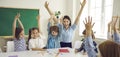 Happy school teacher and little children raising hands up and having fun in class