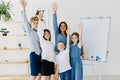 Happy children and educator raising hands up standing in modern classroom. Website header with group portrait of cheerful school Royalty Free Stock Photo