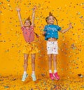 Happy children girls twins on holidays jumping in multicolored confetti on yellow