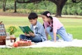 Happy children have a picnic in summer green park garden. Two Asian friends, boy reading book while girl trying to surprise him. Royalty Free Stock Photo