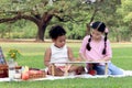 Happy children having a picnic in summer park, cute curly hair African girl with Asian buddy friend studying while sitting on mat Royalty Free Stock Photo