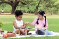 Happy children having a picnic in summer park, cute curly hair African girl with Asian buddy friend studying while sitting on mat Royalty Free Stock Photo