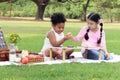 Happy children having a picnic in summer park, cute curly hair African girl with Asian buddy friend studying while sitting on mat Royalty Free Stock Photo