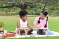 Happy children having a picnic in summer park, cute curly hair African girl with Asian buddy friend studying while sitting on mat Royalty Free Stock Photo