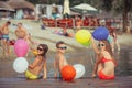 Happy children holding color balloons while sitting on the beach Royalty Free Stock Photo