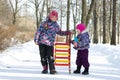 Happy children standing together on a walkway in a snowy winter park an holding the sleds