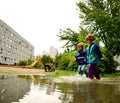 Happy children in water-proof clothes running through the puddle after the rain Royalty Free Stock Photo