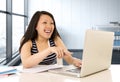 Happy chinese asian woman working and studying on her computer sitting at modern office desk smiling cheerful Royalty Free Stock Photo