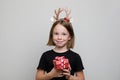 Happy Christmas child girl in hairdeco holds red gift with Xmas ribbon on white background