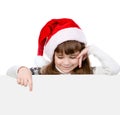 Happy Christmas girl with santa hat looks out from behind a white banner and points down. isolated on white background Royalty Free Stock Photo