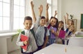 Group of happy school children standing in classroom, raising up their hands and smiling Royalty Free Stock Photo