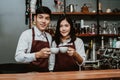 Happy coffee shop small business owner Asian couple wearing in apron holding coffee cups looking at camera while standing at bar Royalty Free Stock Photo