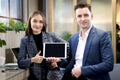 Happy colleague partner businessman and woman showing blank digital tablet at lobby of modern office or coffee shop, attractive Royalty Free Stock Photo