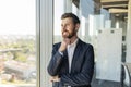 Happy confident businessman in suit standing near window in modern coworking office, waiting for meeting, free space Royalty Free Stock Photo