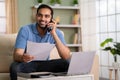 Happy confident indian man talking on mobile phone by holding insurance or property documents at home - concept of Royalty Free Stock Photo