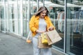 Happy confident smiling plus size curvy young woman with shopping bags walking on city street near shop windows Royalty Free Stock Photo