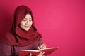 Happy confident successful Asian muslim woman wearing hijab  writing on book, smiling and thinking Royalty Free Stock Photo