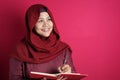 Happy confident successful Asian muslim woman wearing hijab  writing on book, smiling and thinking Royalty Free Stock Photo