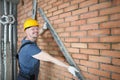 Happy constructor hold metal detail close to brick wall, concrete red wall in empty room