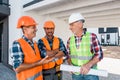 Constructors in helmets standing near coworker with blueprint