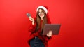 Happy consumer at christmas. Beautiful positive woman in santa hat and red sweater orders gifts on laptop