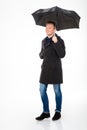 Happy content young male in coat walking under umbrella