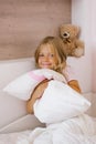 Happy contented girl child sitting on the bed hugging a pillow