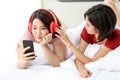 Happy Couple  asia woman wear headphones and enjoy musics playing mobile phone and tablet in bedroom Royalty Free Stock Photo